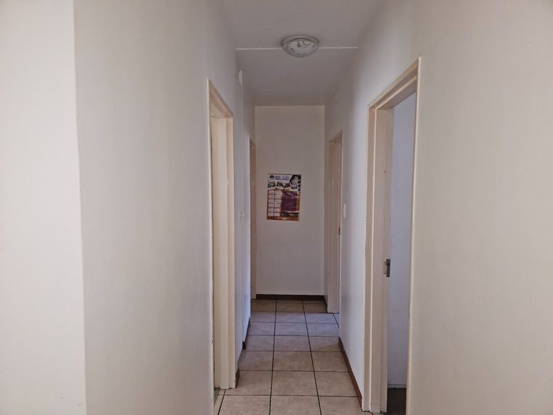 A simple, neutral hallway featuring tiled flooring and multiple doorways leading to other rooms in the apartment.