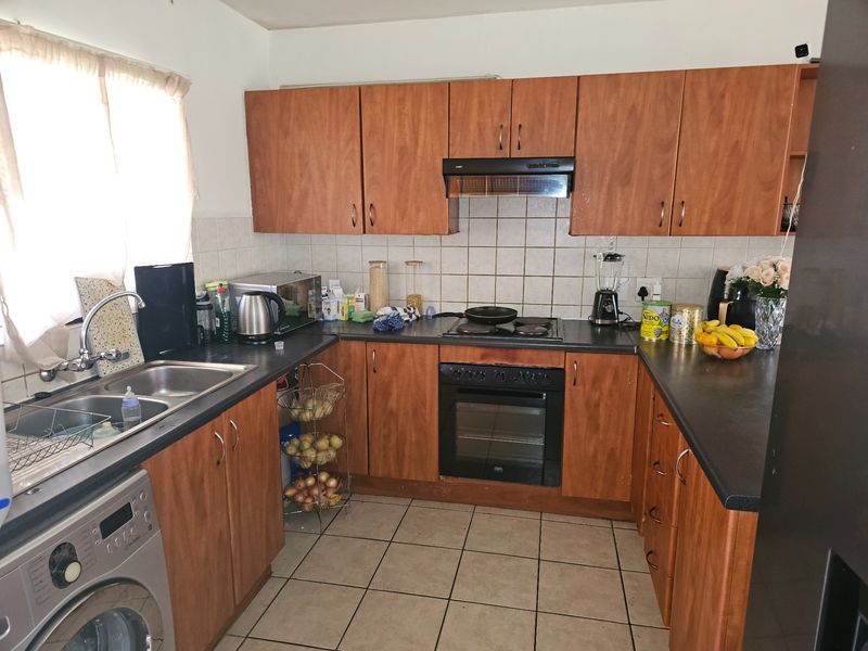 A functional U-shaped kitchen featuring wood-look laminate cabinetry, dark countertops, built-in oven, electric hob, and tiled flooring.