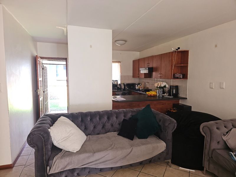 Open-plan living area featuring tiled flooring and a functional kitchen with wood-finish cabinetry, leading directly to the exterior entrance.