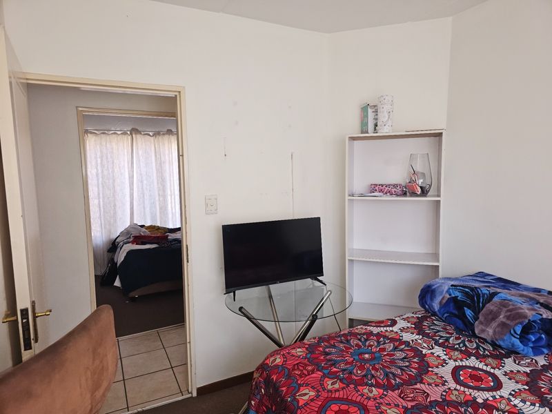 A bedroom interior featuring a built-in shelving unit, with a doorway leading to an adjacent room with tiled flooring.