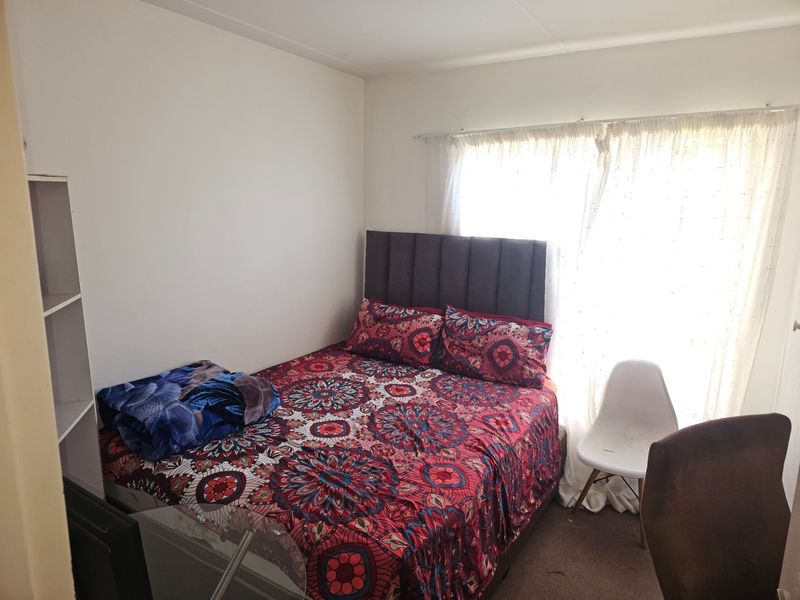 A standard bedroom featuring neutral walls, carpeted flooring, and a window with curtain treatments.