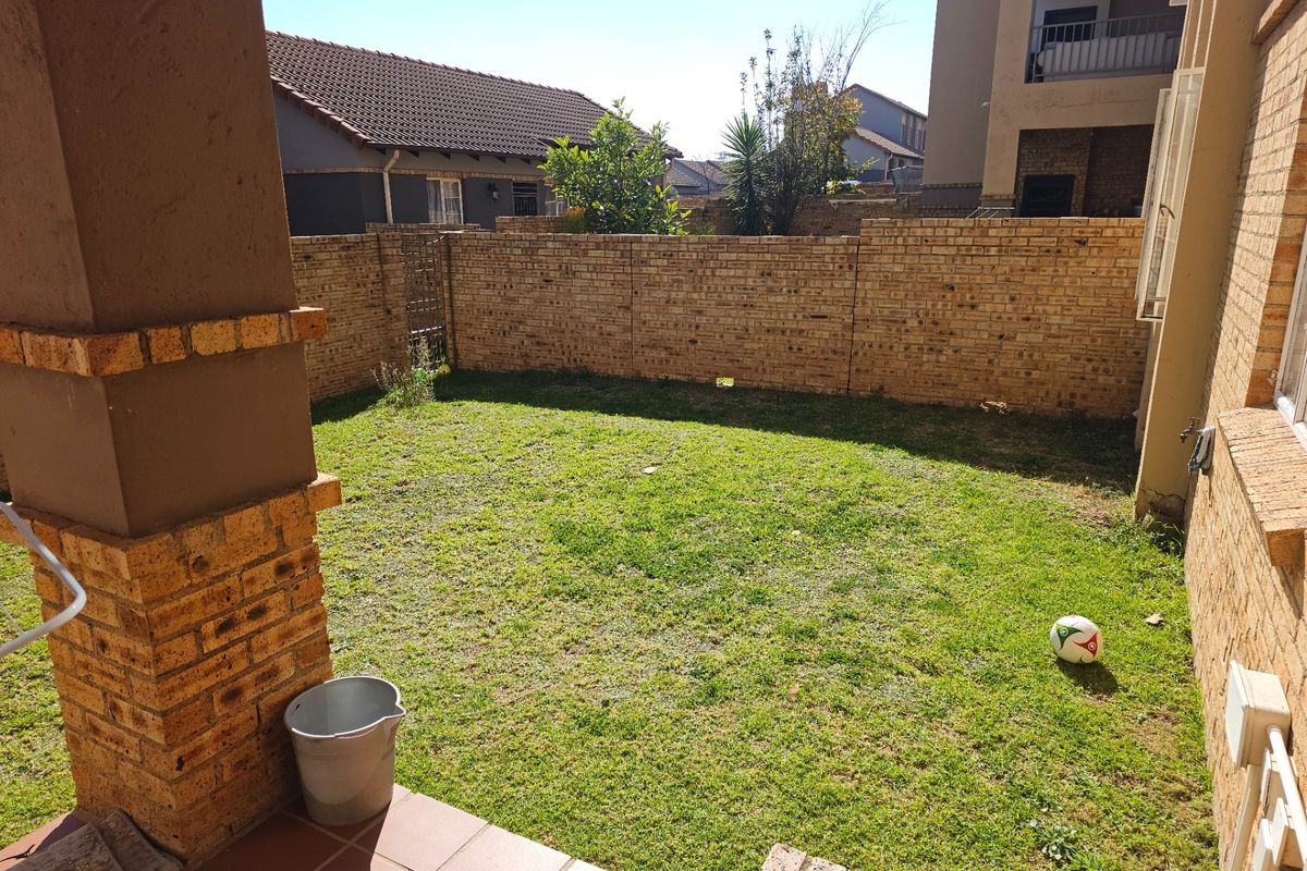 A private rear garden featuring a small lawn area, enclosed by a brick boundary wall, with an adjacent tiled patio space.