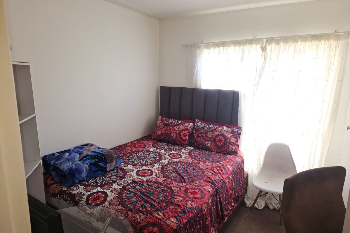A standard bedroom featuring neutral walls, carpeted flooring, and a window with curtain treatments.