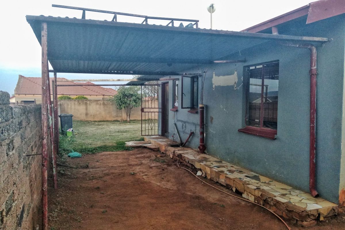 Rear exterior view of the property featuring a metal carport structure, stone-paved walkway, and access to the backyard area.