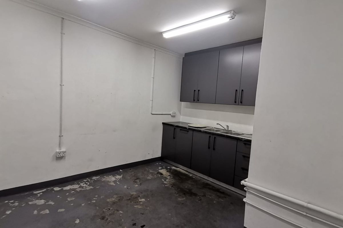 A functional utility or kitchenette area featuring dark grey cabinetry, a stainless steel sink, and industrial-style surface-mounted lighting and electrical conduits.