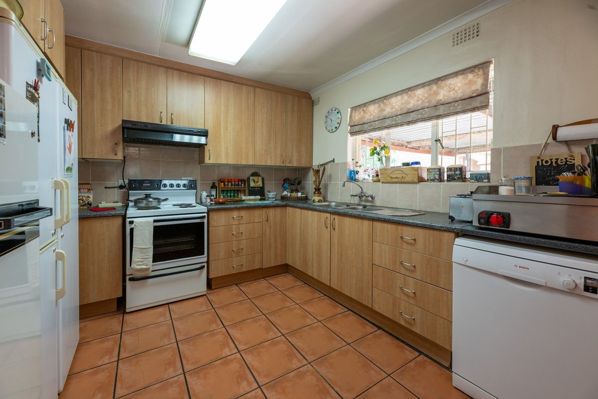 A functional kitchen featuring light wood-look cabinetry, laminate countertops, a freestanding stove with extractor fan, and terracotta floor tiles.