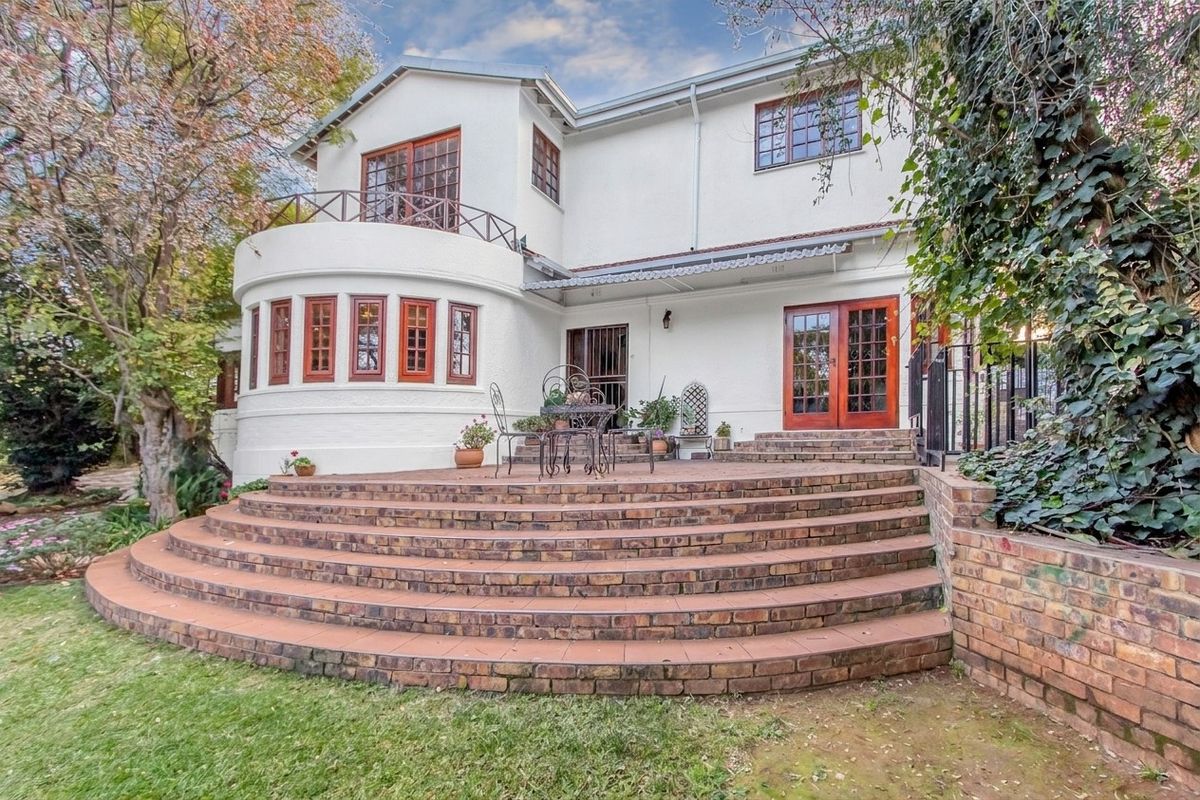 Rear elevation of a two-story house featuring a large curved brick patio, wooden window frames, and a balcony overlooking the garden.