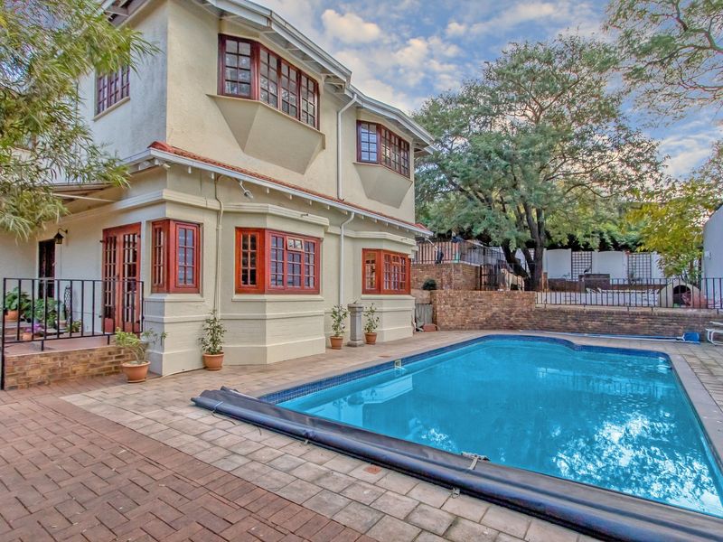 A well-maintained rear garden area featuring a swimming pool, brick paved patio, and a multi-story residence with classic casement windows.