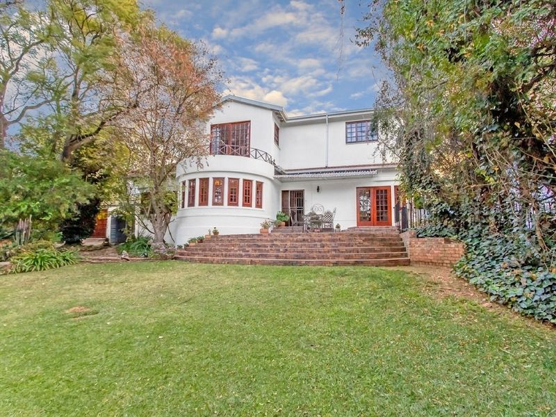 Rear view of a two-story house featuring a brick staircase leading to a patio, timber-framed windows, and a spacious garden area.