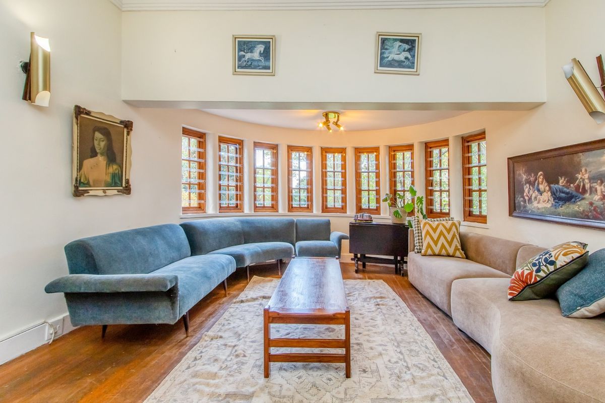 A spacious living room featuring a distinctive curved wall with multiple timber-framed windows, hardwood flooring, and wall-mounted accent lighting.