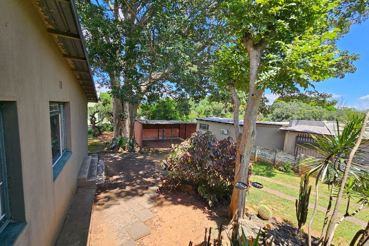 A view of the rear garden area featuring mature trees, a lawn, and a secondary outdoor structure or shed.
