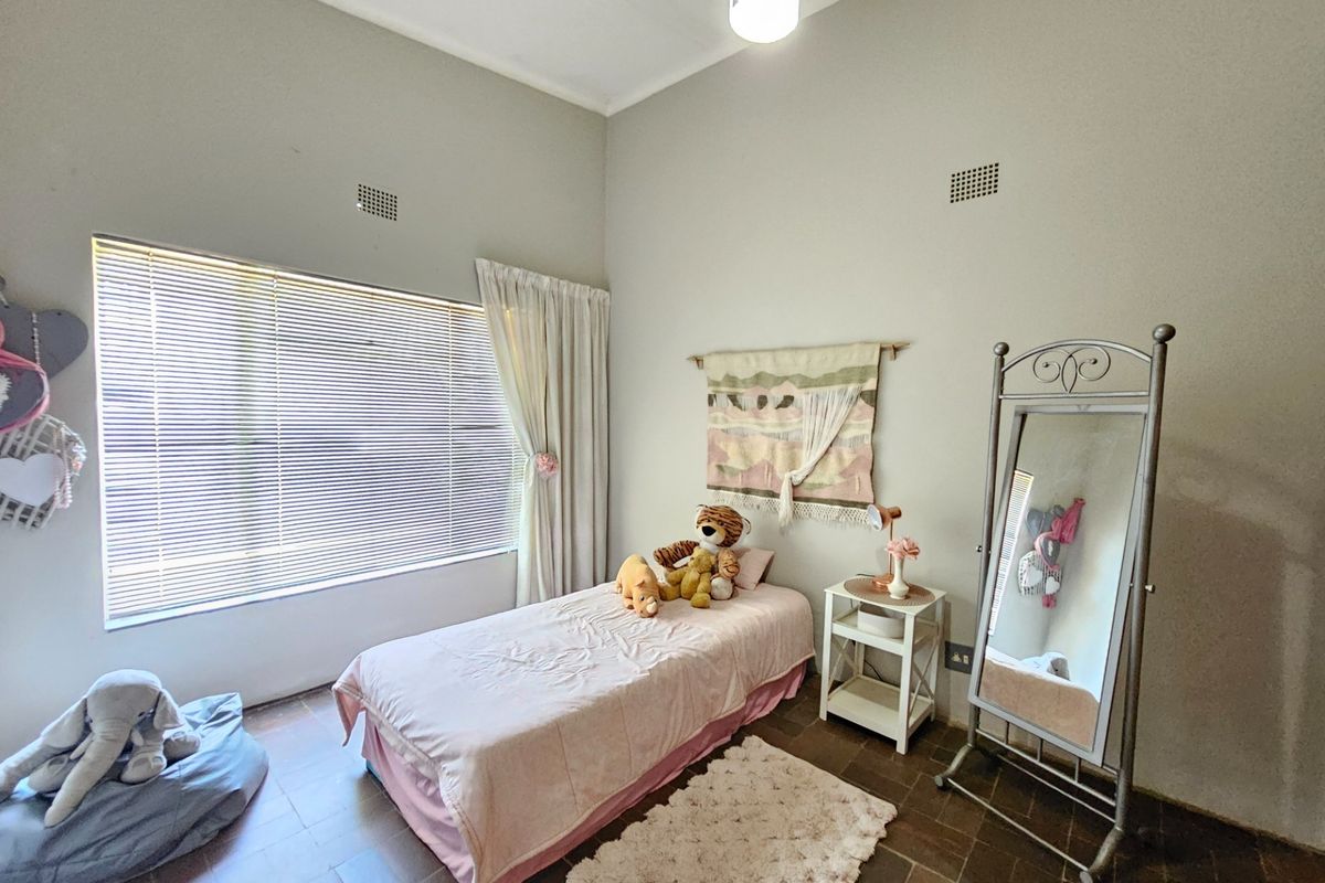 A bright bedroom featuring high ceilings, tiled flooring, and large windows with fitted blinds, offering a comfortable and functional living space.
