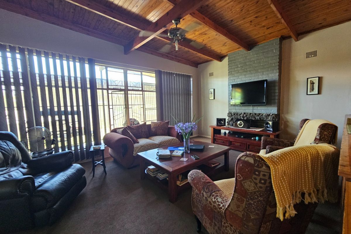 Spacious living room featuring a high vaulted timber ceiling, exposed beams, and a prominent stone-clad fireplace with integrated television mount.