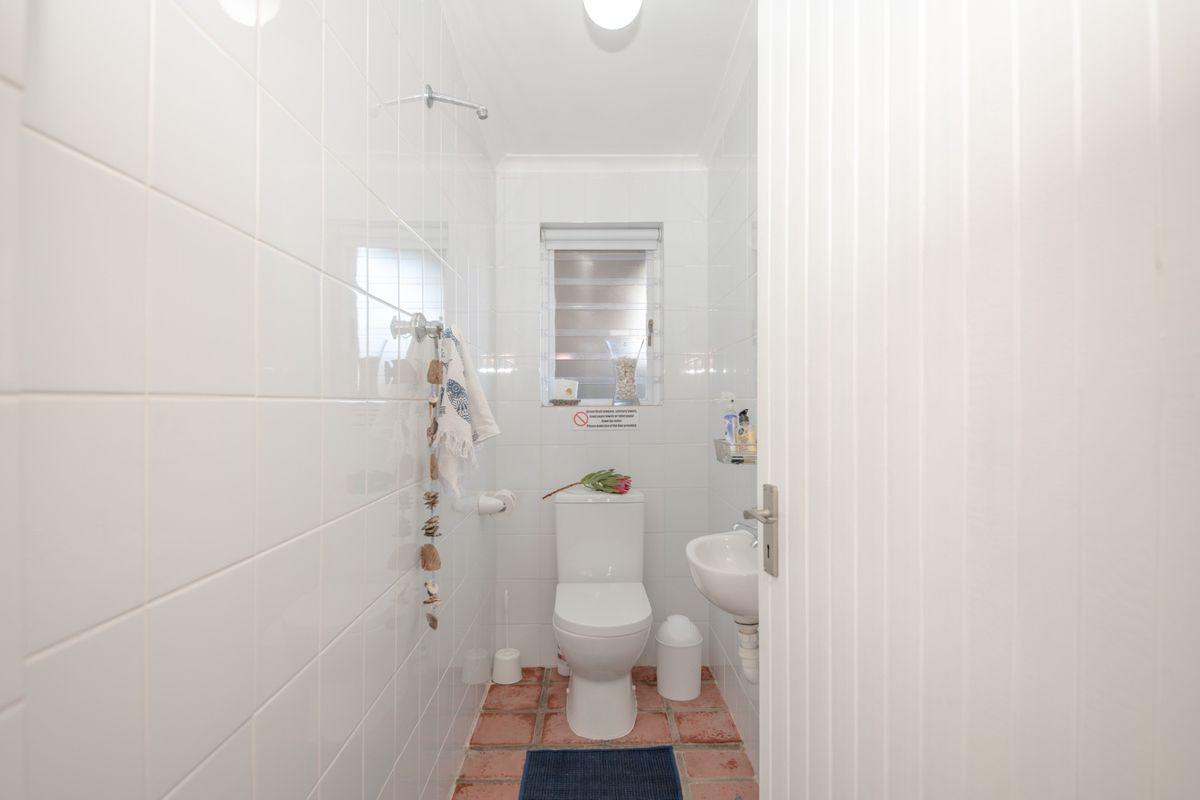 A compact bathroom featuring white wall tiles, a standard toilet, a small wall-mounted basin, and terracotta floor tiles.