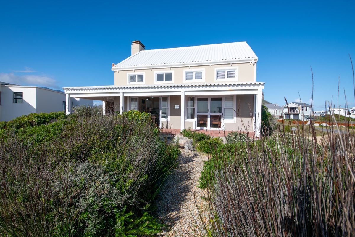A rear view of a two-story house featuring a covered patio, white corrugated metal roof, and a landscaped garden path.