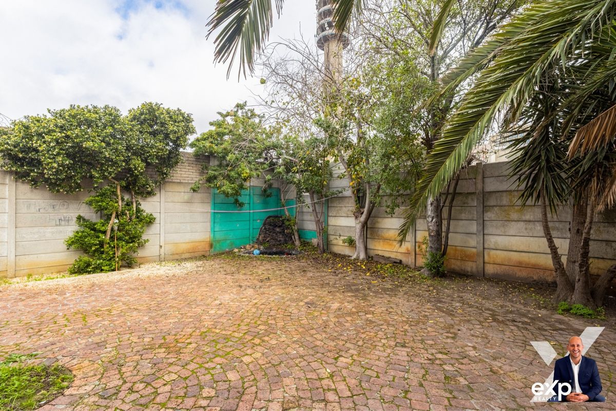A private rear garden area featuring paved flooring, mature trees, and a high boundary wall with a gated access point.