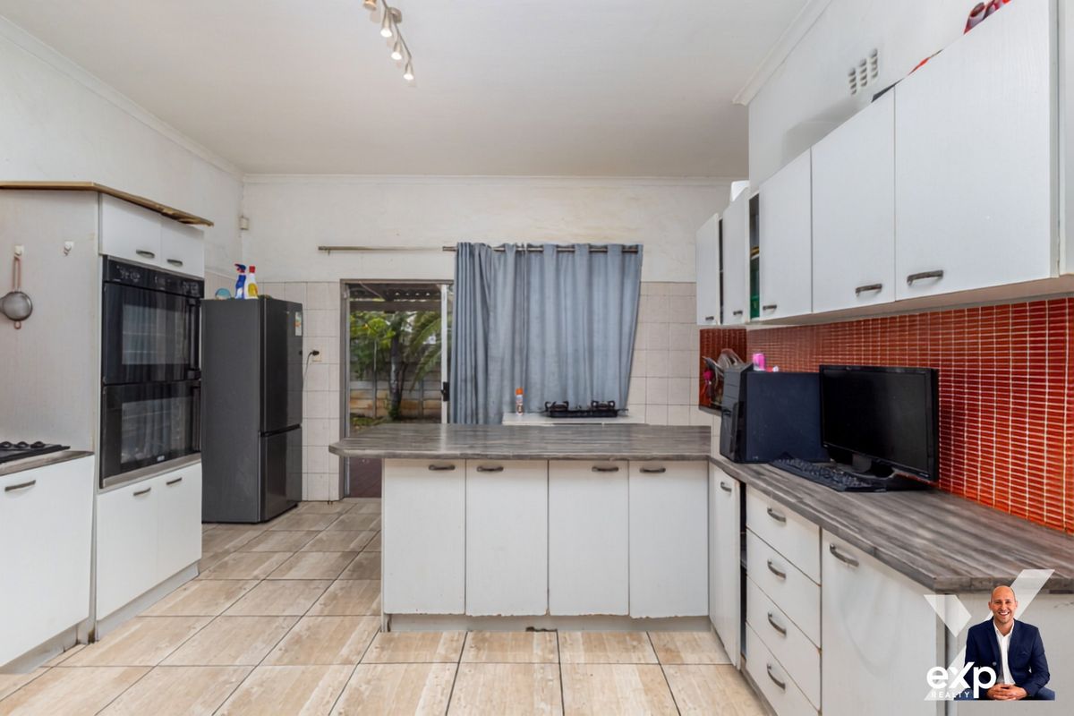 Functional kitchen featuring built-in double oven, laminate countertops, white cabinetry, and tiled flooring with direct access to the rear exterior.