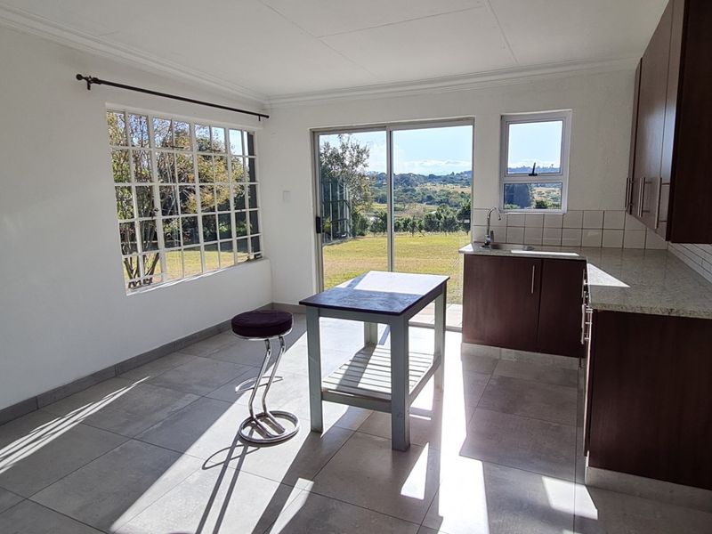 Bright open-plan kitchen and living area featuring modern tiled floors, dark wood cabinetry, stone countertops, and large sliding doors opening to a scenic garden view.