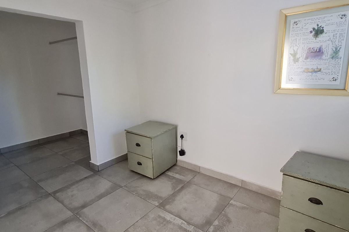A bright bedroom featuring neutral tiled flooring and a convenient walk-in closet area with built-in hanging rails.
