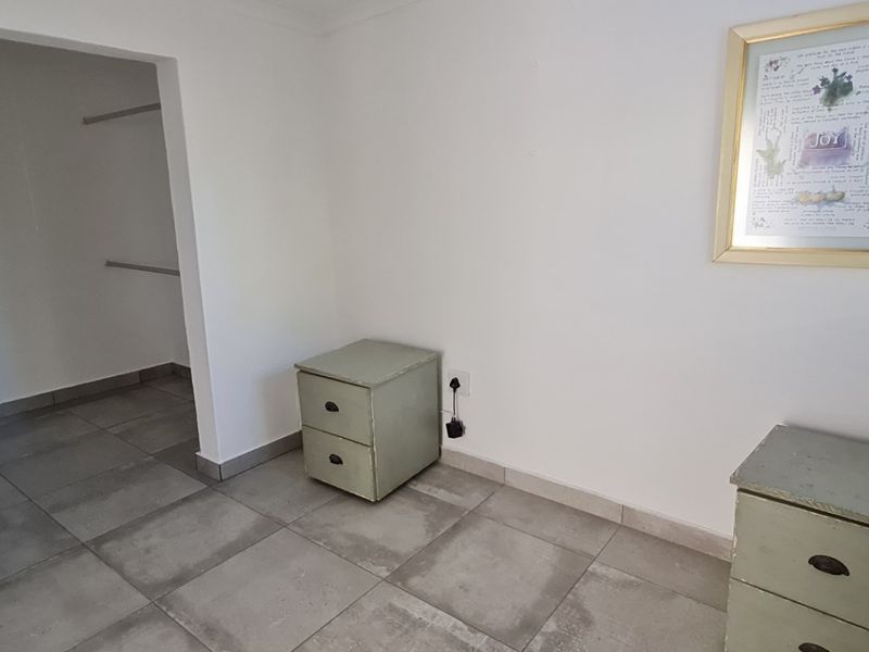 A bright bedroom featuring neutral tiled flooring and a convenient walk-in closet area with built-in hanging rails.