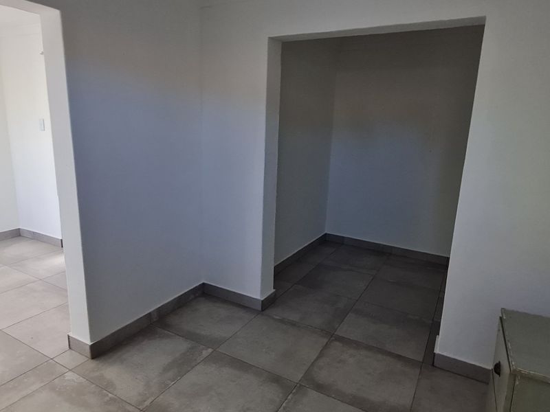 A bright, neutral hallway featuring large format floor tiles and clean white walls, providing a seamless transition between living spaces.