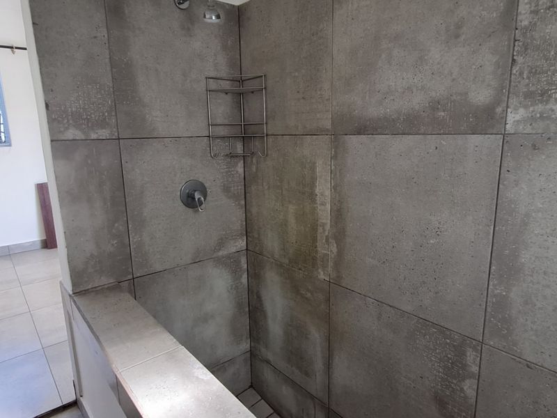 A bathroom featuring a walk-in shower with concrete-look wall tiles and tiled flooring, presenting a functional space with potential for cosmetic updates.