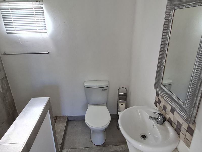 A clean, functional bathroom featuring a pedestal basin, toilet, and tiled shower area with neutral finishes and natural light.