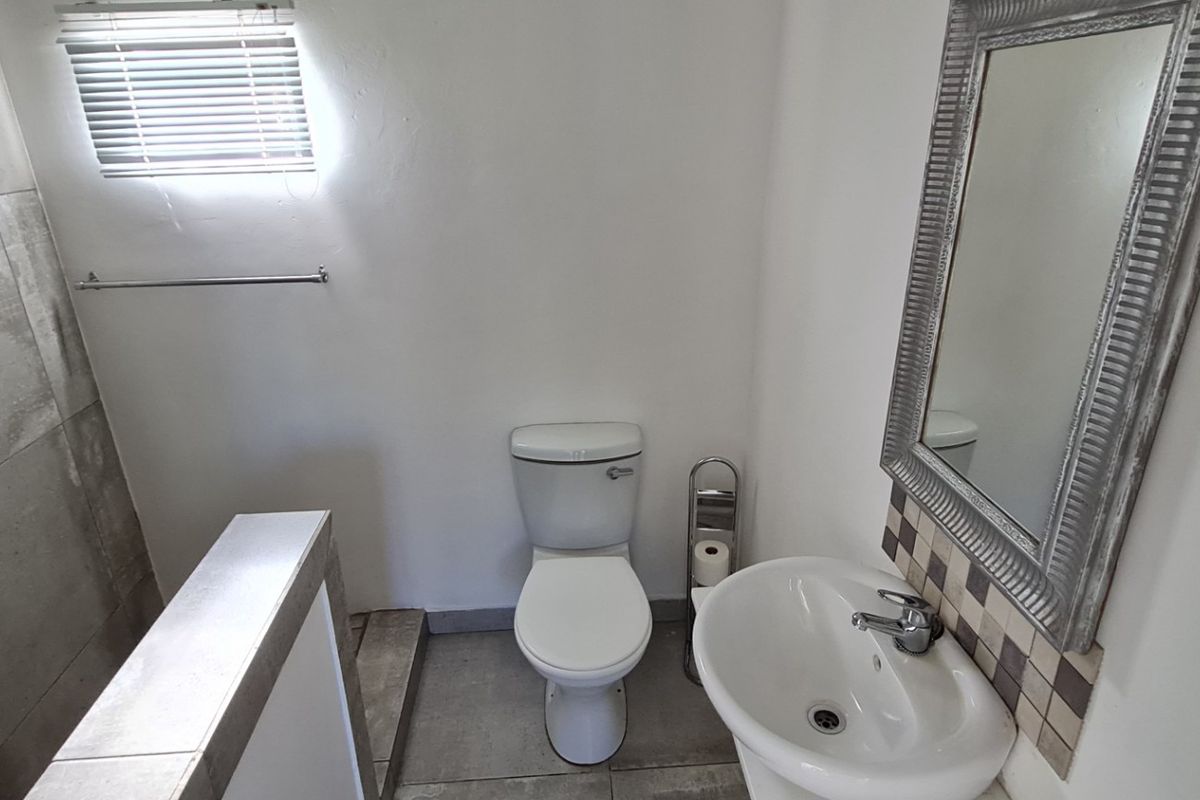 A clean, functional bathroom featuring a pedestal basin, toilet, and tiled shower area with neutral finishes and natural light.
