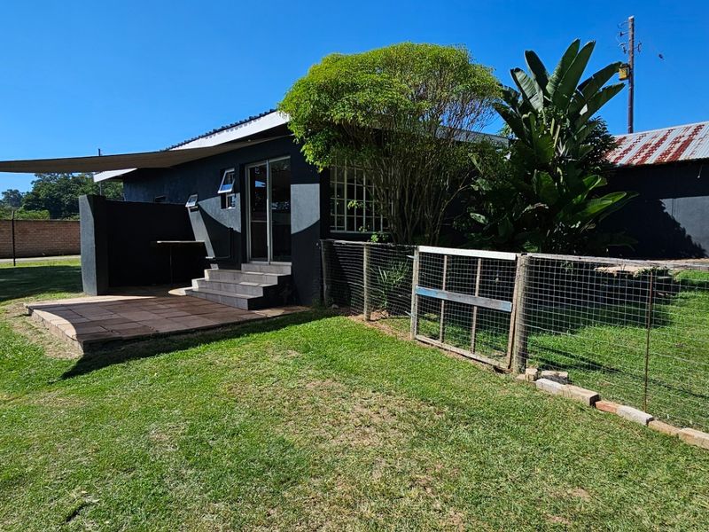 Rear view of the cottage featuring a tiled patio area, shade sail, and surrounding garden space with wire mesh fencing.