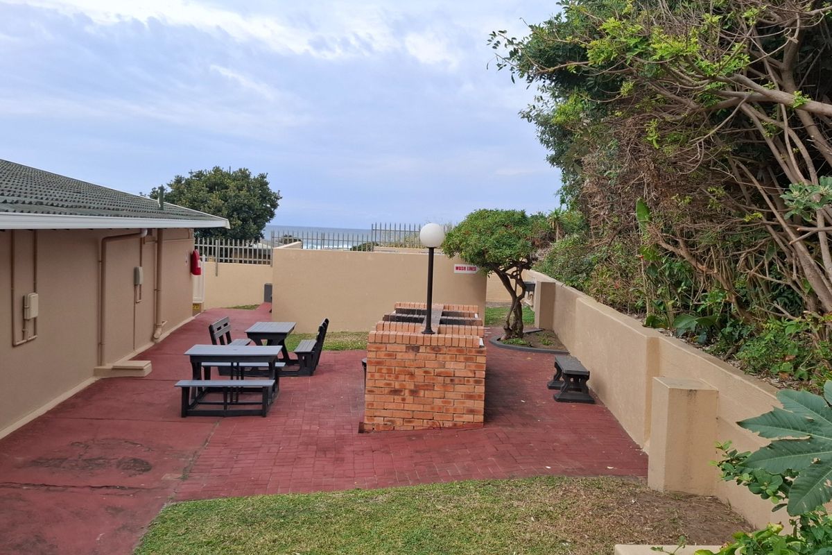 Outdoor communal area featuring a brick-built barbecue station, paved patio space, and perimeter boundary walls with ocean views in the distance.