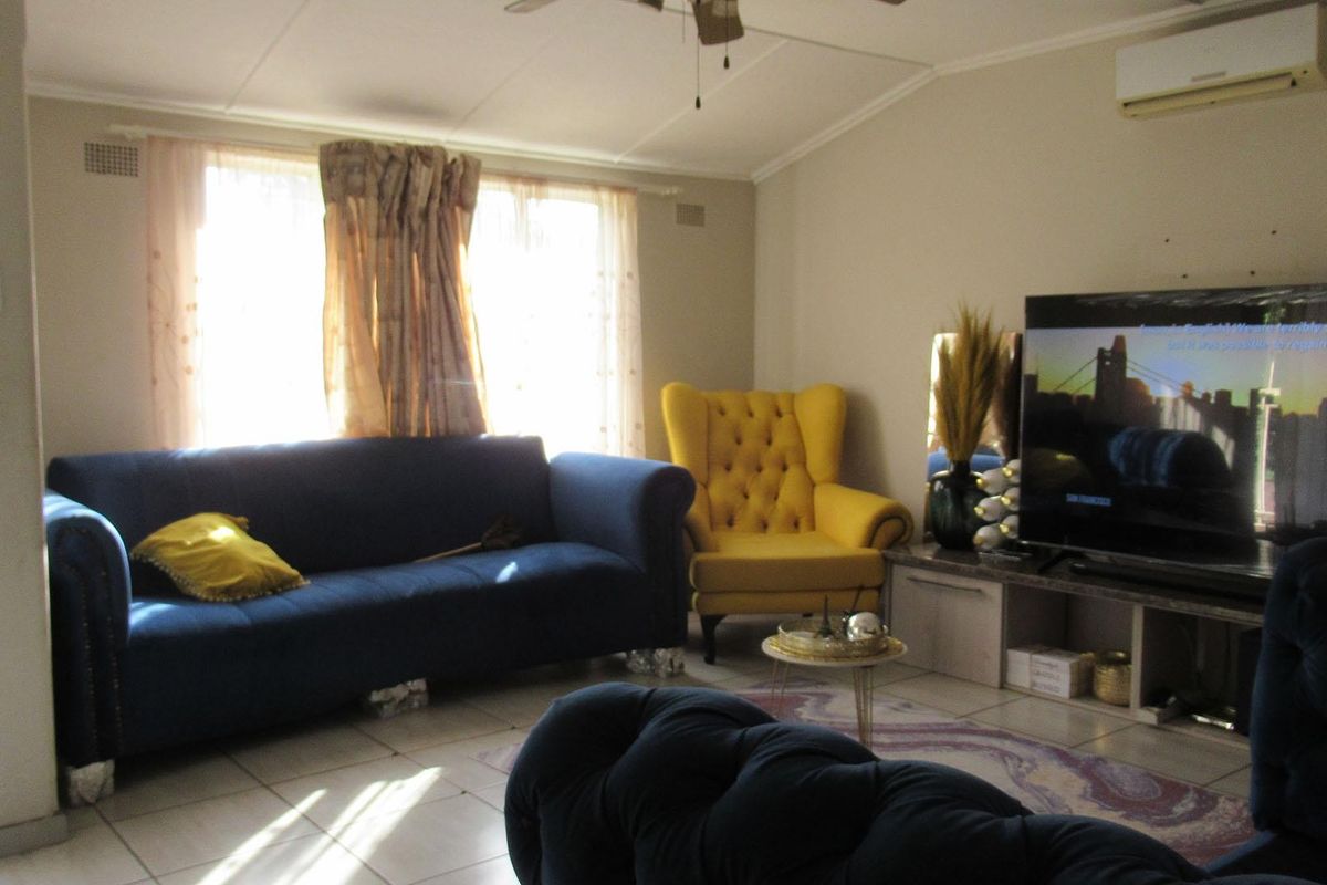 A living room featuring tiled flooring, a wall-mounted air conditioning unit, and a ceiling fan.