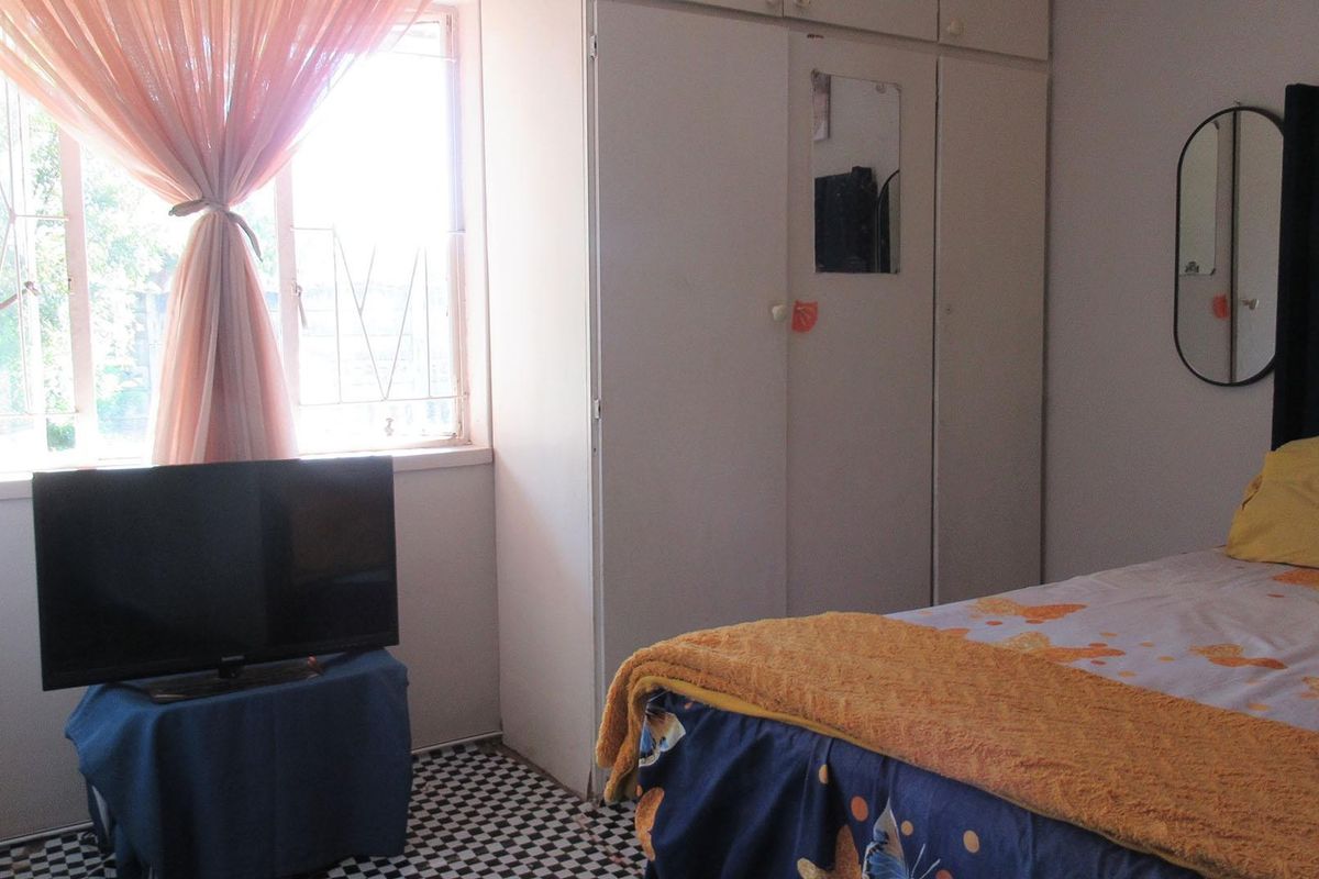 A functional bedroom featuring built-in cupboards and a window with security bars, providing natural light and storage space.