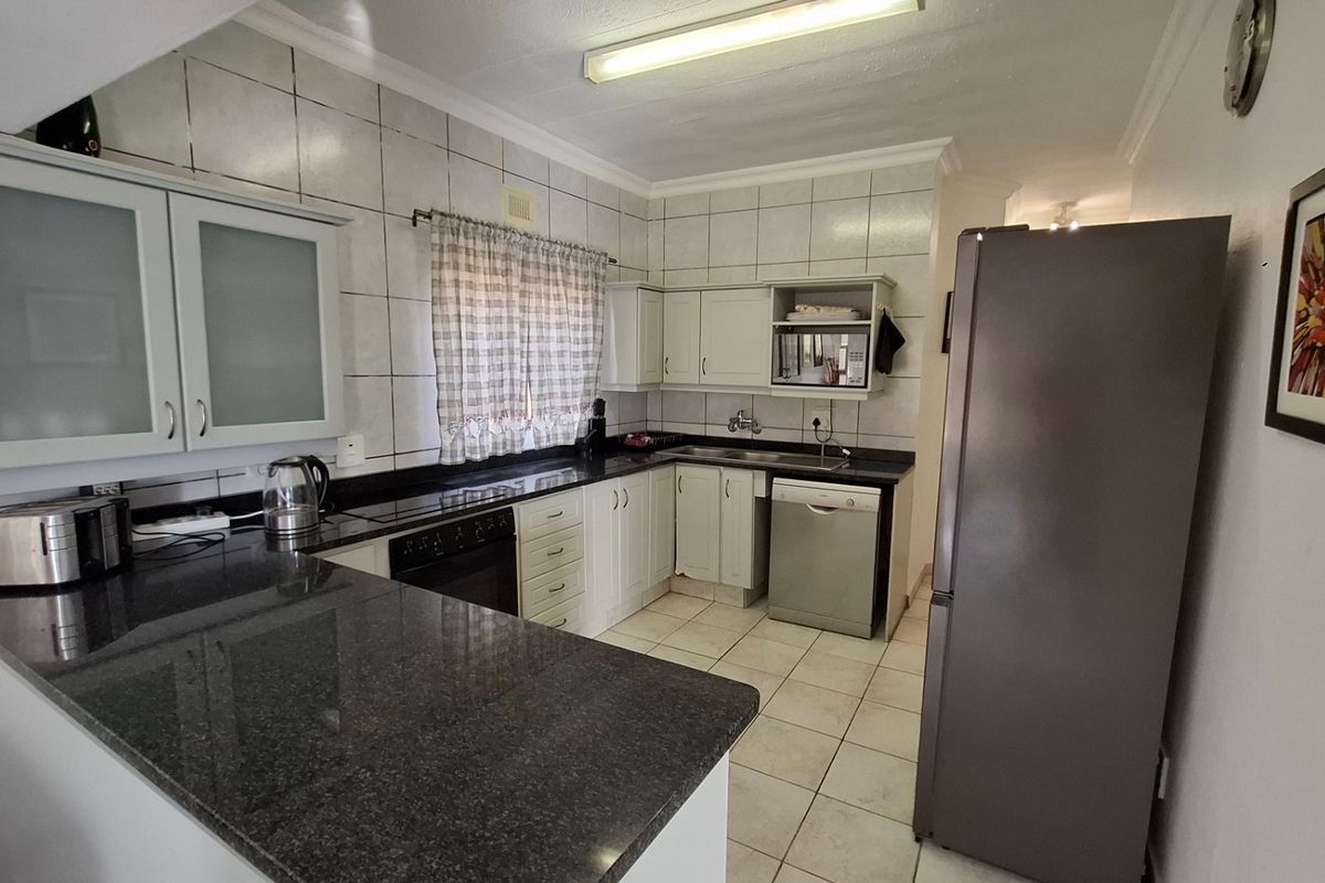 A functional kitchen featuring granite countertops, white cabinetry, tiled splashbacks, and integrated appliance spaces, offering a practical layout for daily meal preparation.