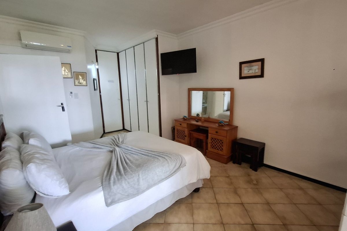 A bedroom featuring built-in cupboards, tiled flooring, and a wall-mounted air conditioning unit.