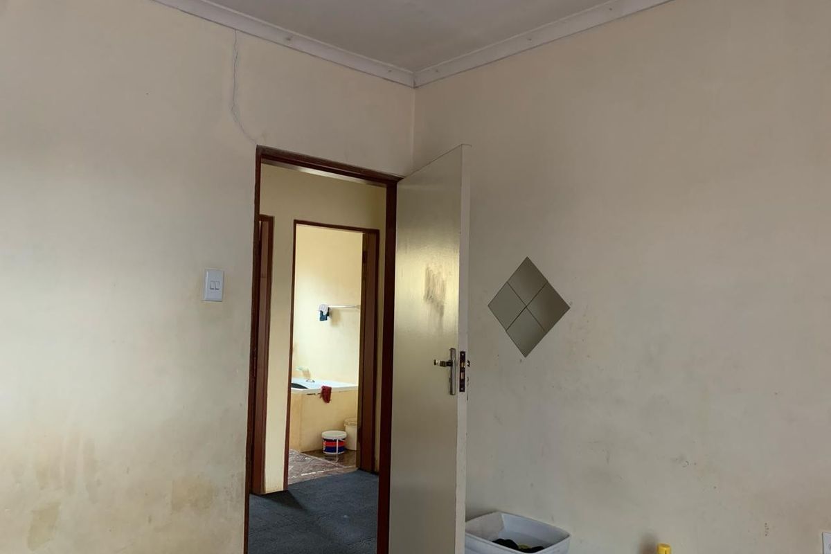 A bedroom interior showing signs of wear, including wall cracks and surface staining, with an adjacent view into a bathroom area.