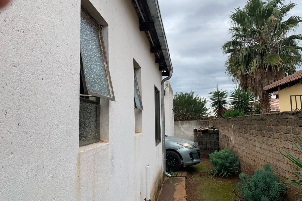 Side exterior view of the house showing the building facade, metal window frames, and a narrow garden area with a brick boundary wall.