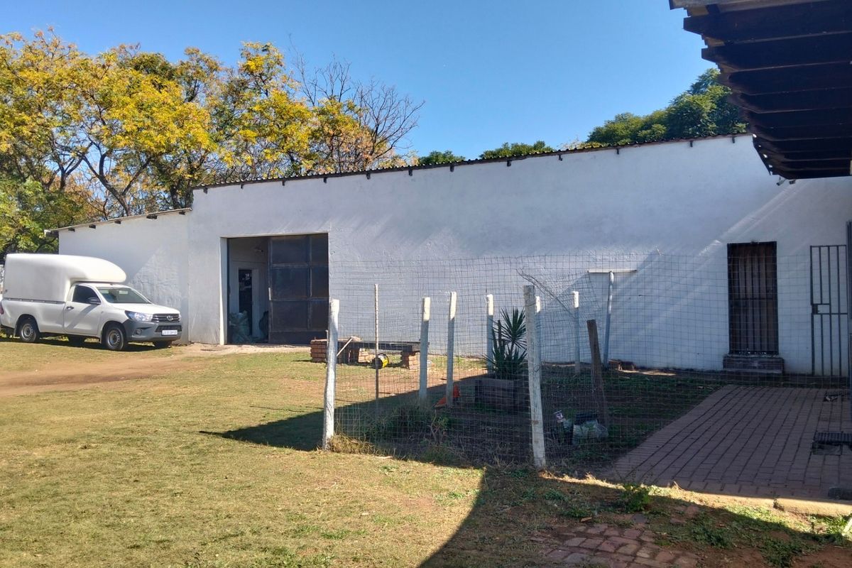 Exterior view of a large outbuilding or workshop structure on a small holding, featuring a wide entrance and adjacent fenced garden area.
