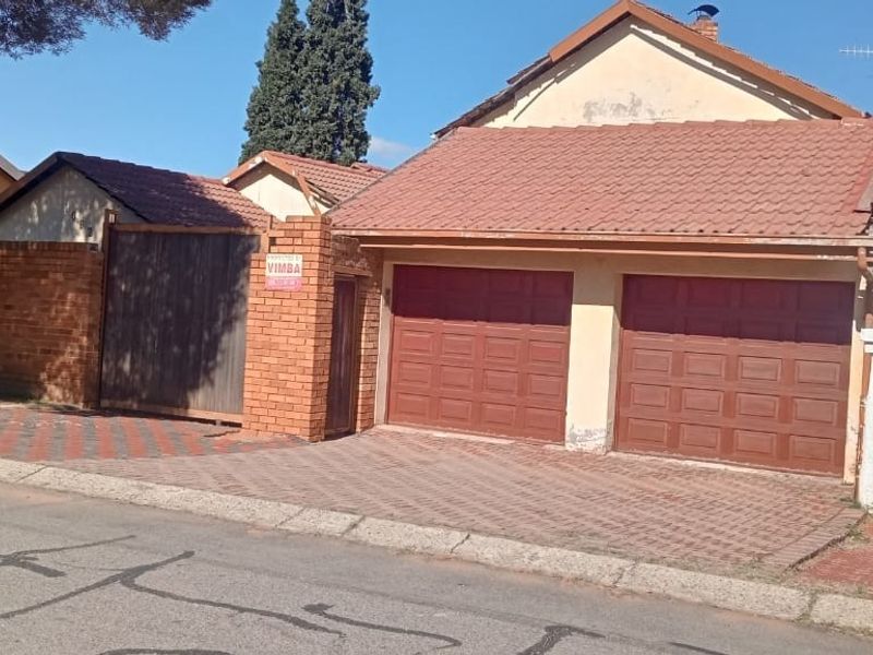 Street view of the property featuring a double garage with paved driveway, brick boundary wall, and gated entrance.