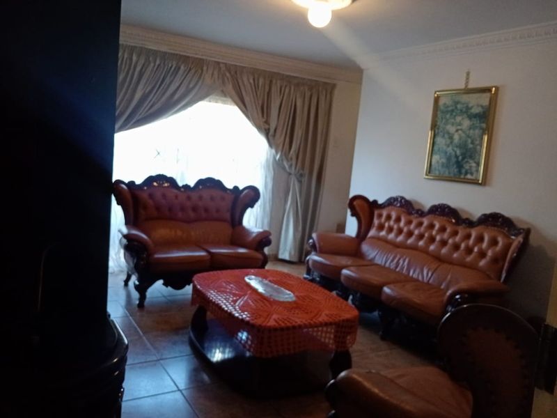 A living room featuring tiled flooring, decorative ceiling cornices, and large windows with curtains.