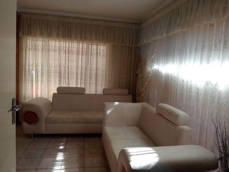 A living room featuring tiled flooring and large windows covered by layered curtains, providing natural light to the space.