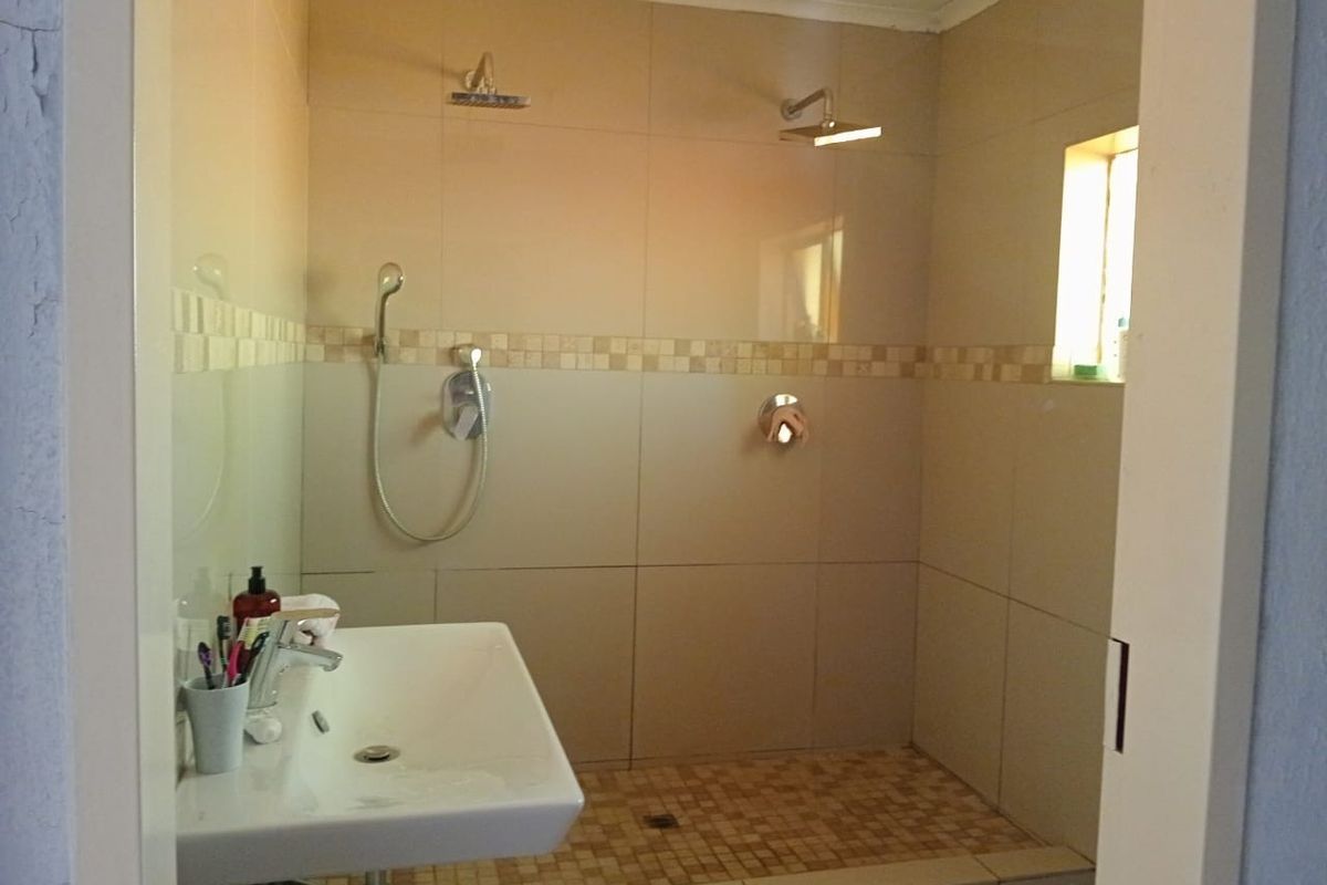 A functional bathroom featuring a walk-in shower with dual shower heads, a wall-mounted basin, and neutral wall tiling with a decorative mosaic border.
