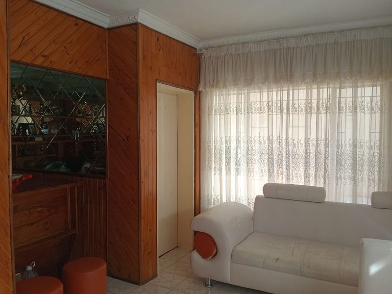 Living room featuring dated wood wall paneling, tiled flooring, and a built-in bar area with decorative mirror detailing.