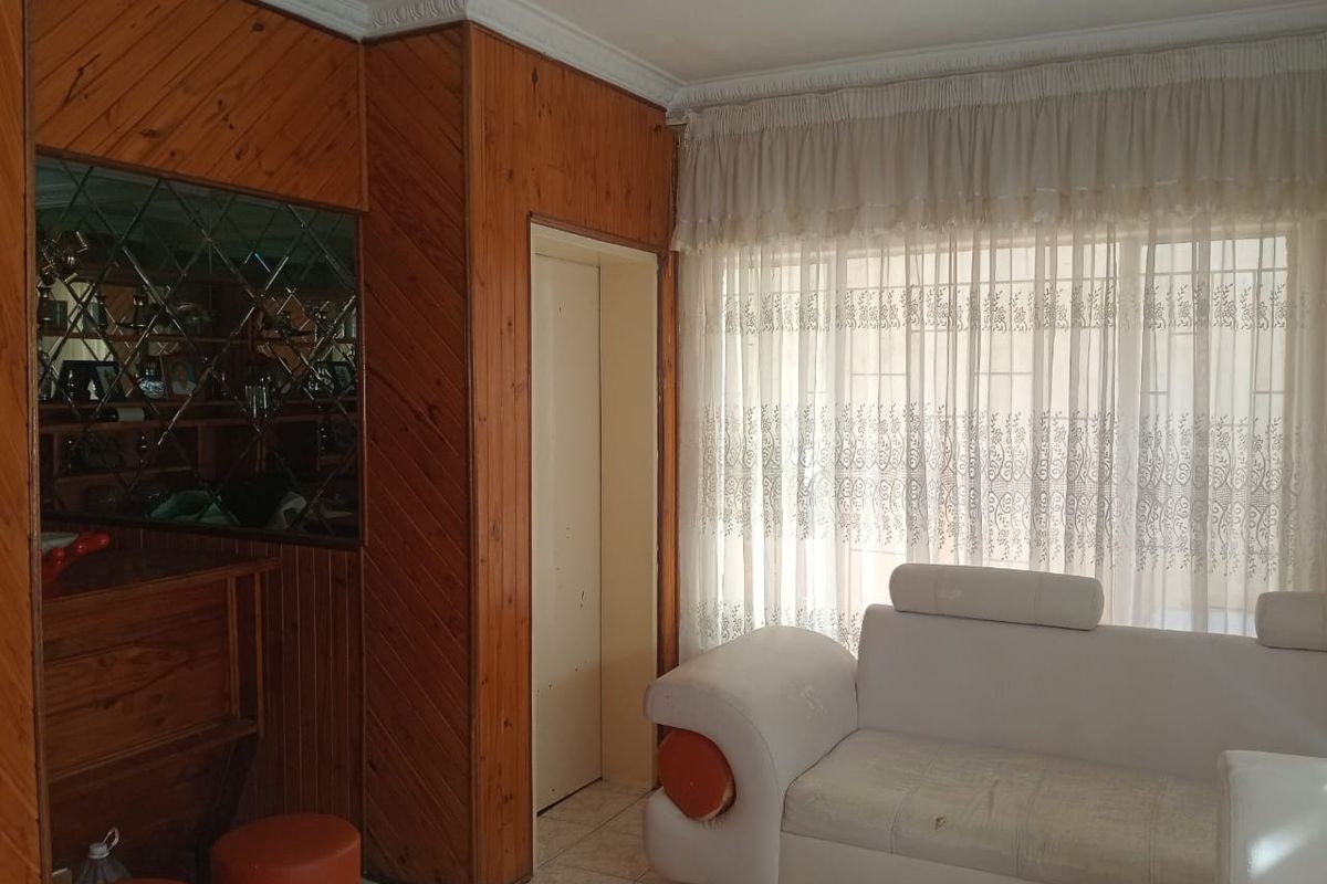 Living room featuring dated wood wall paneling, tiled flooring, and a built-in bar area with decorative mirror detailing.