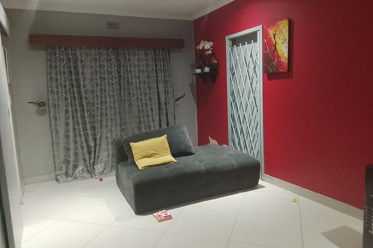A living room featuring tiled flooring, a security gate, and recessed lighting, currently showing signs of wear including peeling paint on the wall.