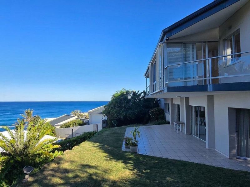 Rear view of the property featuring a tiled patio, glass balcony railing, and expansive ocean views.