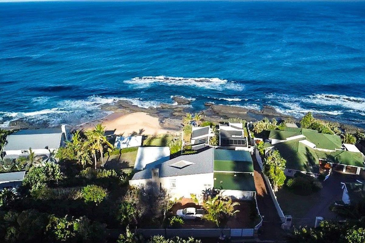 Aerial view of a coastal residential property featuring multiple buildings, green roofing, and direct proximity to the ocean shoreline.