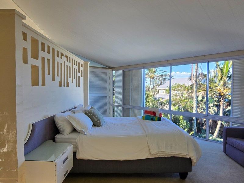 Spacious bedroom featuring a unique decorative partition wall, large floor-to-ceiling windows with natural light, and views of the surrounding greenery and ocean.