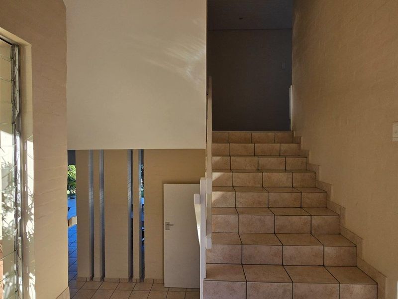 A bright entrance hallway featuring tiled stairs, a large glass window, and a clean, neutral interior design.