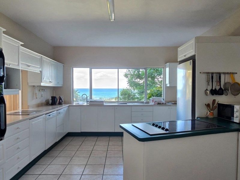 A functional kitchen featuring white cabinetry, a built-in oven, a cooktop, and a large window offering scenic ocean views.