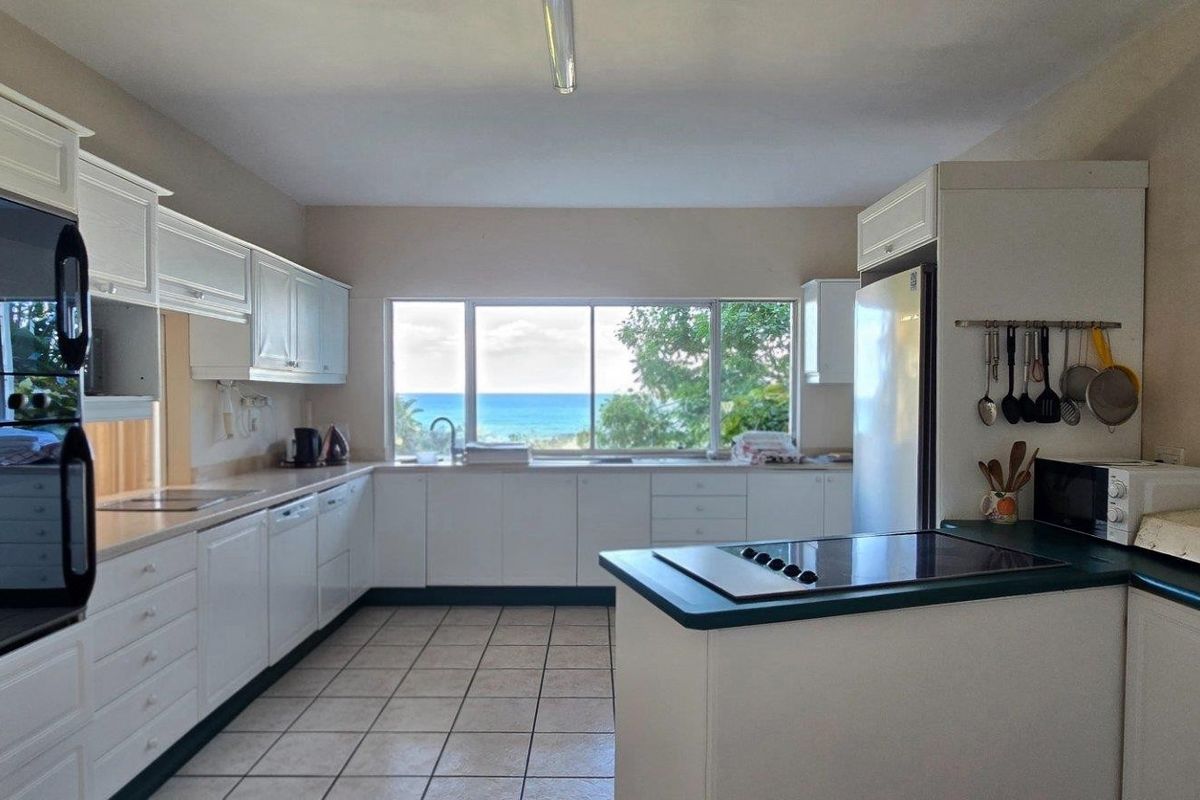 A functional kitchen featuring white cabinetry, a built-in oven, a cooktop, and a large window offering scenic ocean views.